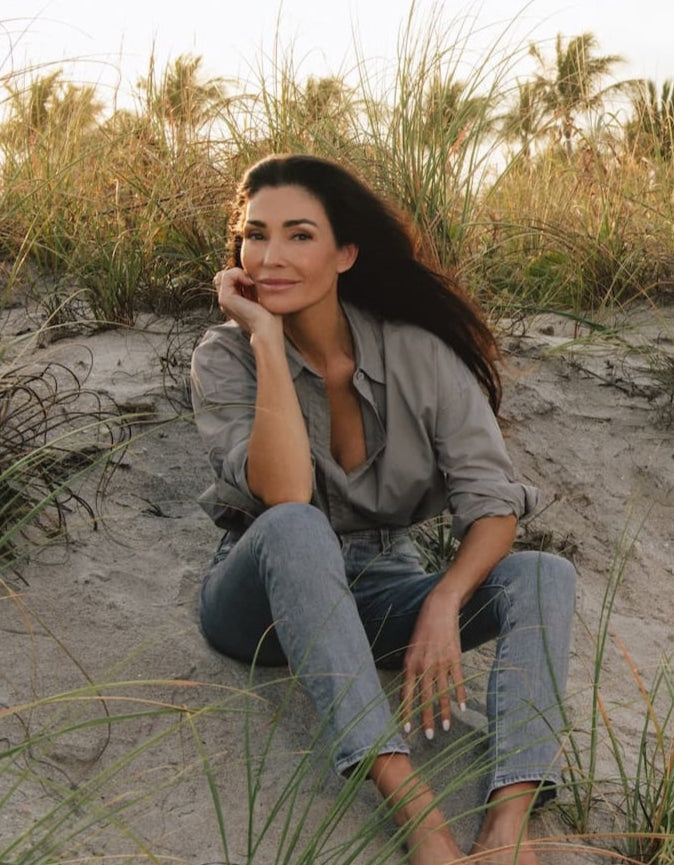 Dara sitting on a sandy beach with grasses around