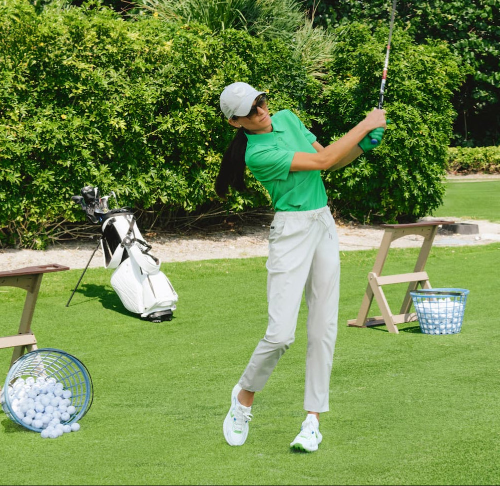 Woman playing golf on a green course with trees in the background