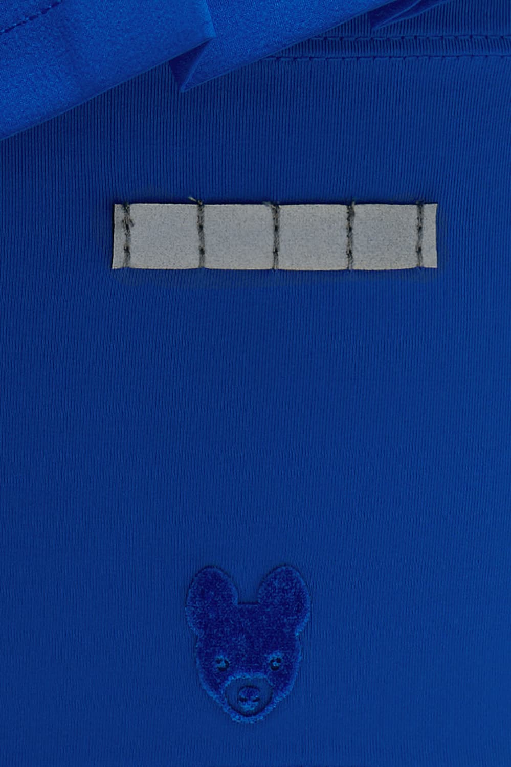 Color:Blu Close-up of a royal blue fabric garment, likely a shirt or jacket, featuring a horizontal row of five rectangular silver reflective tee holder and a small embroidered dog head motif below.